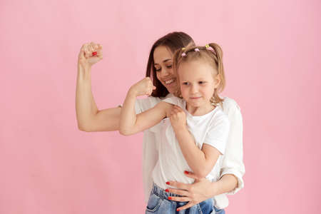 Funny family on the background of a bright pink wall. Mother and her daughter little girl having fun, showing that the strength of the muscles. Woman power, feminismの写真素材