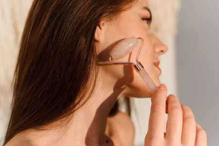 Young woman with fresh radiant skin doing a spa facial at home. Natural Jade Face Lift Roller, Rejuvenating Facial Massageの写真素材