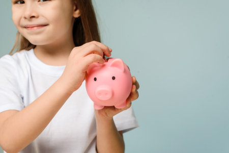 A little girl puts a coin in a piggy bank. The concept of teaching children personal finance and saving.の写真素材
