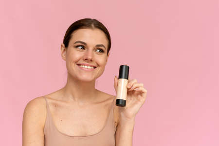 A young woman holds a foundation in a tube on a pink background. Makeup advertisingの写真素材