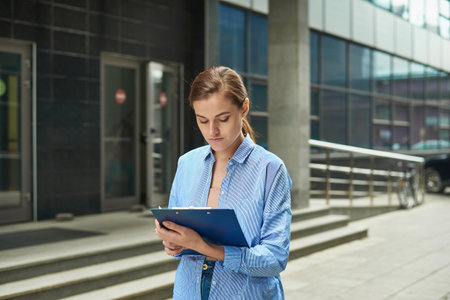 Professional young lawyer woman standing in front of court and holding legal documents waiting for customers ready to handle case. Outdoorの写真素材