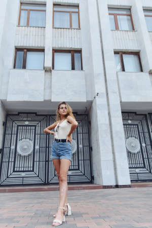 Stylish vertical urban portrait of a young woman against the backdrop of a tall building. Woman Teenager Portrait Hipster Style Conceptの写真素材
