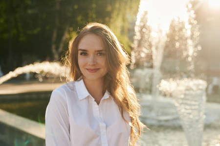 Lovable long-haired blonde woman enjoying life and having fun at resort. Beautiful portrait of a young girl in a white shirt.の写真素材