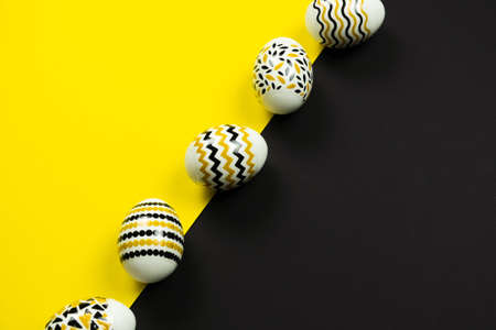 Golden, black, white eggs with a geometric pattern on a yellow and black background. View from above. Easter card with copy space for text.の写真素材