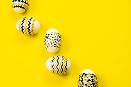 Golden, black, white eggs on a yellow background. View from above. Easter card with copy space for text.の写真素材