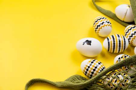 Golden, black, white eggs in a string bag on a yellow background. View from above. Easter card with copy space for text.の写真素材