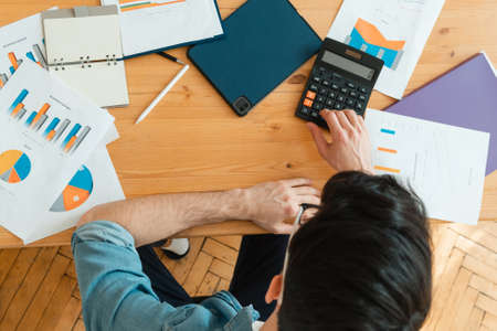 A young man sorts out household finances in the living room. Investments, buying an apartment and running your own business.の写真素材