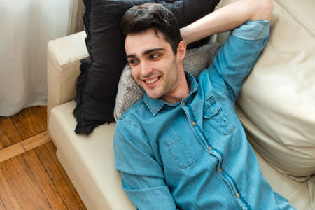Young handsome man is relaxing on the sofa at home and thinking about the future. Caucasian millennial lies on the sofa, relaxes and looks away.の写真素材