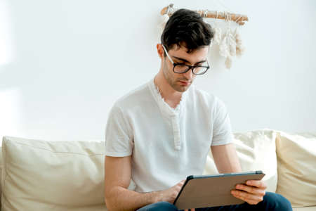 Portrait of a male freelancer who is always in touch at home. Handsome focused young man using his smartphone while sitting on the couchの写真素材