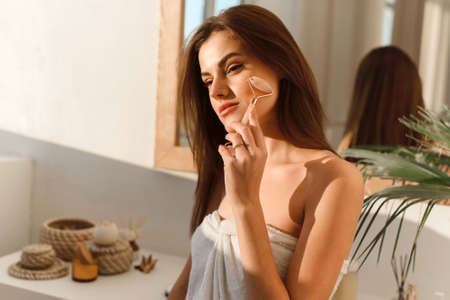 Young woman with clean beautiful skin makes massage with a jade roller for the face. Home spa. Skin care.の写真素材