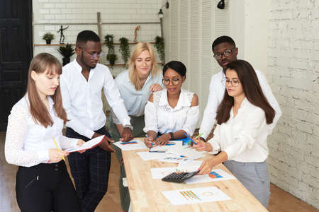 A team of multiethnic people are discussing business in the office. The employees of the company communicate, looking at the schedules and discussing the further strategyの写真素材
