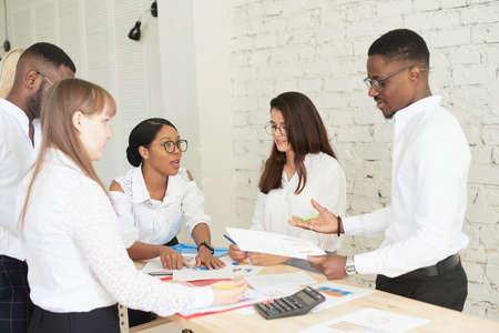 A team of multiethnic people are discussing business in the office. The employees of the company communicate, looking at the schedules and discussing the further strategyの写真素材