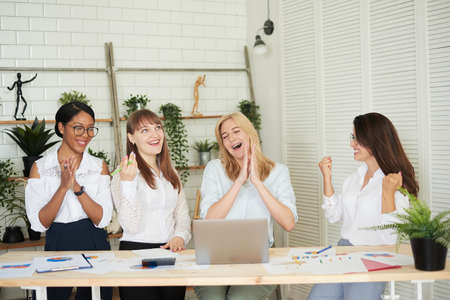 Emotional businesswomen, multiethnic company members scream with joy, feel happy, achieve business goal, sign important contract, realize worthy project, happy winner concept moment in officeの写真素材