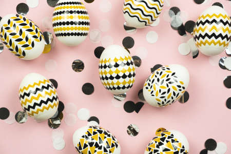 Easter composition. Gold, black Easter eggs with geometric design, confetti on pastel pink background. Flat lay, top viewの写真素材