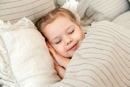 Charming little girl sleeps in bed. Little blonde sleeps sweetly in bed with white linen. place for text. healthy childの写真素材