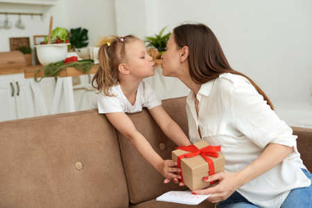 A young mother kisses her daughter and thanks her for the gift and the card.の写真素材