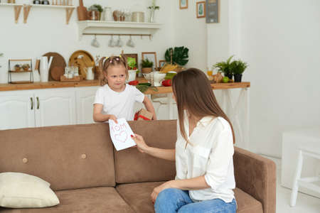 A cute little girl gives a handmade card with a heart to her mom.の写真素材