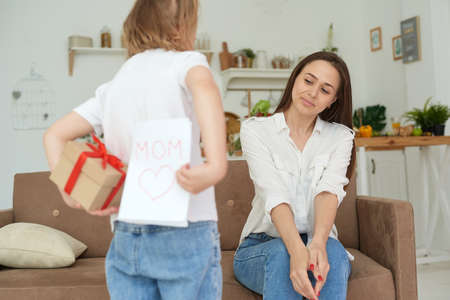 Lovely little girl gives her mom a card and a gift for March 8 or mothers day. Loving family concept.の写真素材