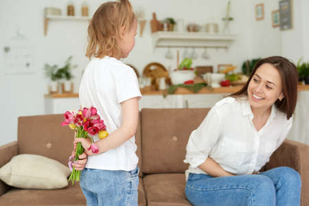 Adorable preschooler girl giving bouquet of tulip flowers to excited mom, family celebrating birthday or mothers dayの写真素材