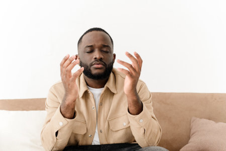 A black Muslim man prays while sitting on a couch.の写真素材