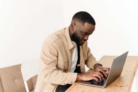 Focused african american man working on laptop from home. Black freelancer programmer works at the table.の写真素材