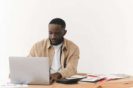 Focused african american man working on laptop from home. Black freelancer programmer works at the table.の写真素材