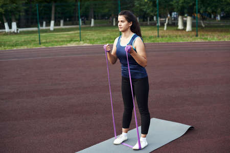 Young woman shakes muscles in her arms using an expander and fitness elastic bands. beautiful young sportswoman training with stretching bandの写真素材