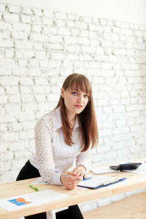 A business woman stands at a table with business reports and looks into the cameraの写真素材