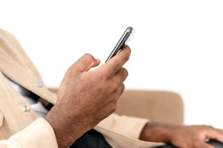 A close shot of an African American mans hand browsing the news or social media feed on his phone while sitting on the couch at home. Phone in the hand of a black man. Rest and relaxationの写真素材