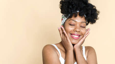 Smiling lovely african american woman touching face skin and smiling on beige background. The concept of natural beauty, beautiful skin. Web bannerの写真素材