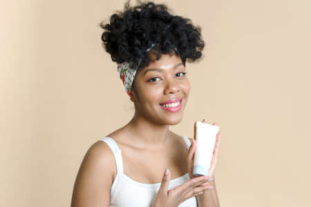 Portrait of african american woman holding skin care moisturizer and smiling. Attractive black woman with beautiful skin holding a bottle of cosmetic cream mockup.の写真素材