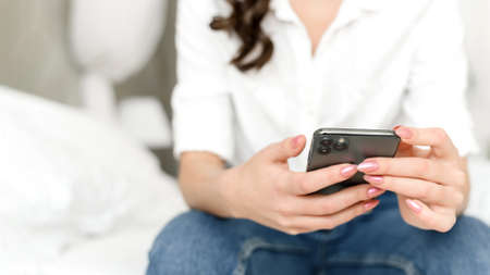 Close up of a womans hands with a mobile phone in the bedroom on the bed. Web banner.の写真素材
