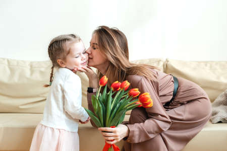 Postcard for March 8. Little daughter kisses and hugs mother with yellow flowers, tulips. Mothers Dayの写真素材