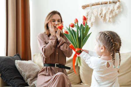 Happy daughter congratulates mom with tulips at home in the living room.の写真素材