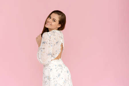 Smiling young enjoying caucasian woman in a summer dress on a pink background. Charming lady in white outfit posing with a happy expression.の写真素材