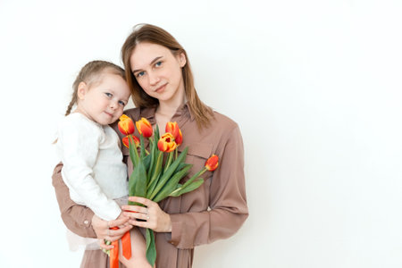 Happy daughter congratulates mom with tulips. Portrait. Looking at cameraの写真素材