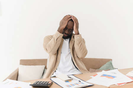 Problems in the household budget during the crisis. Young black sad man looking through mortgage papers or economic reports, upset and angry.の写真素材