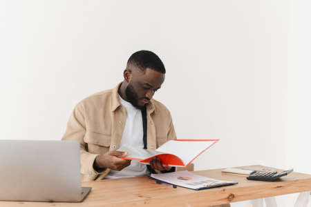 Serious african american man reading notes in business paperwork while sitting at home and working on economic projectの写真素材