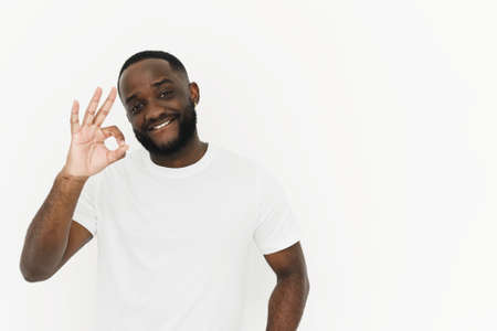 Smiling african american young man in white t-shirt showing ok gesture on white background with copy...