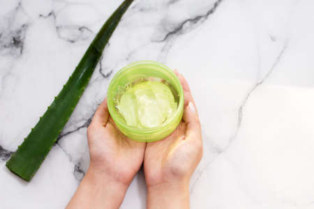 Female hands holding aloe gel on marble backgroundの写真素材