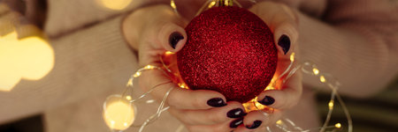 Womens hands in a sweater hold a Christmas ball with garland lights. New year and christmas concept. Copy space, web bannerの写真素材