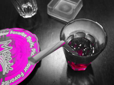 A pink fluorescent drink with a colored straw on a bar table with other objects                     ...