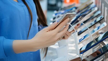 Young woman chooses a new mobile phone in an electronics store
