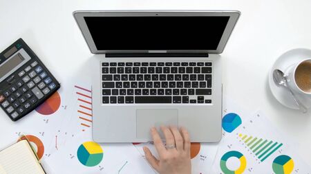 Top view minimal workspace, Woman hand working on laptop calculator, With coffee cup, Notebook, On white wooden desk.の写真素材