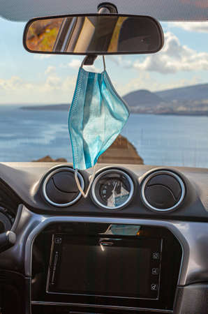 Surgical mask hanging from the rearview mirror of the car, parked at the seaの写真素材