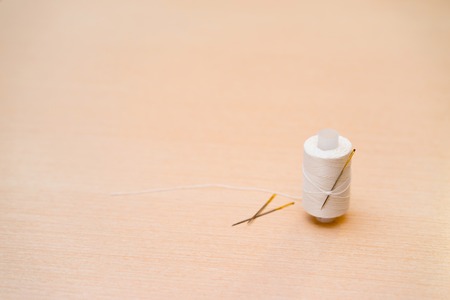 a spool of white thread with needle in the backgroundの写真素材