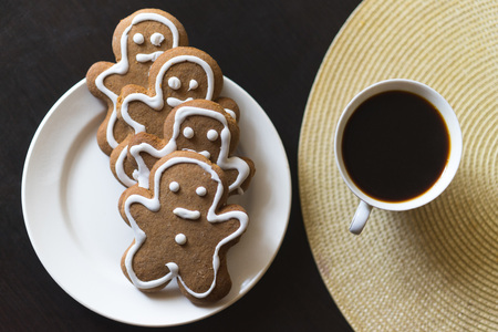 gingerbread men on a white plate on black background with a cup coffee.