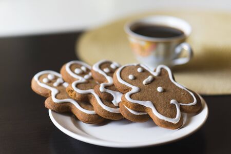 gingerbread men on a white plate on black background with a cup coffee.