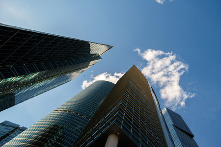Underside angle view to background of modern glass building skyscrapers over blue sky. City of Moscowの写真素材