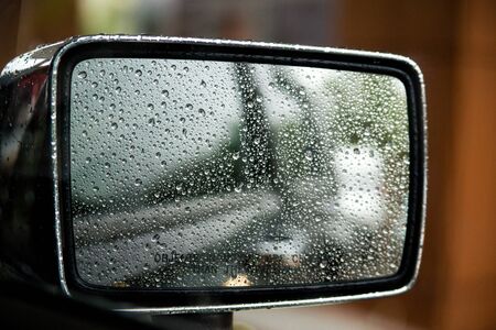 Raindrops on car mirror with side wing mirror. Rainy day on the road